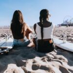 Beach - a couple of women sitting on top of a sandy beach