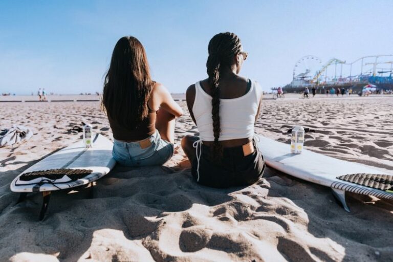 Beach - a couple of women sitting on top of a sandy beach
