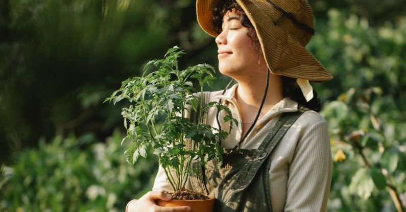 Cultivating Mindfulness - Content ethnic female grower in panama hat with potted plant and closed eyes in summer garden