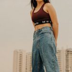Fitness Trends - Full body of young female wearing sport top and denim with sneakers standing on rooftop of modern building