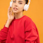 Celebrity Trends - Woman in Red Sweatshirt and Blue Jeans Wearing White Headphones