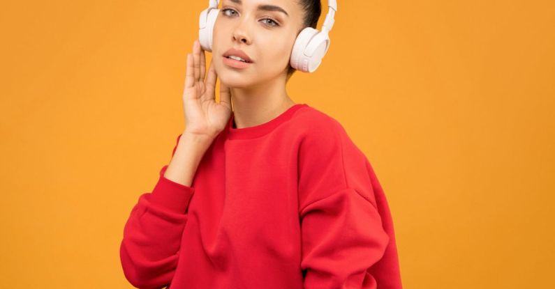 Celebrity Trends - Woman in Red Sweatshirt and Blue Jeans Wearing White Headphones