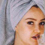 Natural Skincare - Young woman with hair wrapped with towel and bared shoulders drinking water and looking at camera