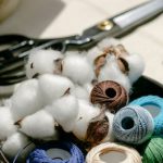 DIY Fashion Designers - Thread bobbins with scissors and needles placed on table in atelier