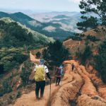 Weekend Getaway - Back view of unrecognizable hikers with trekking poles traveling in green hilly valley