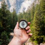 Travel Health - person holding compass facing towards green pine trees