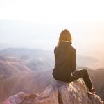 Mountain Retreats - person sitting on top of gray rock overlooking mountain during daytime