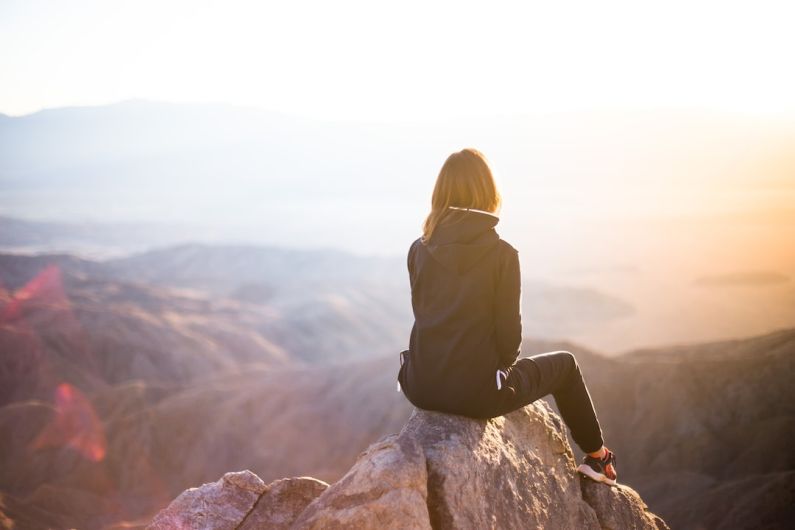 Mountain Retreats - person sitting on top of gray rock overlooking mountain during daytime