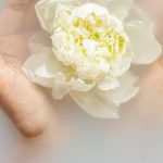 Organic Beauty - Unrecognizable female with soft manicured hands holding white flower with delicate petals in hands during spa procedures