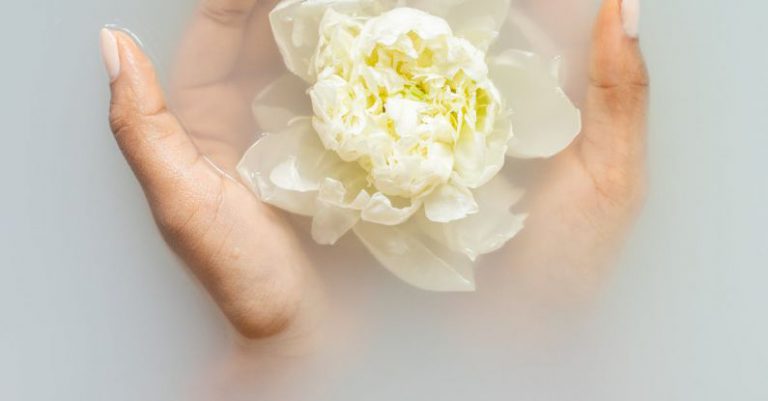 Organic Beauty - Unrecognizable female with soft manicured hands holding white flower with delicate petals in hands during spa procedures