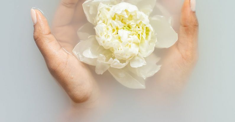 Organic Beauty - Unrecognizable female with soft manicured hands holding white flower with delicate petals in hands during spa procedures