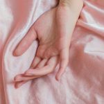 Sensitive Skin - Top view of hand of crop anonymous female on soft silk creased bed sheet at home