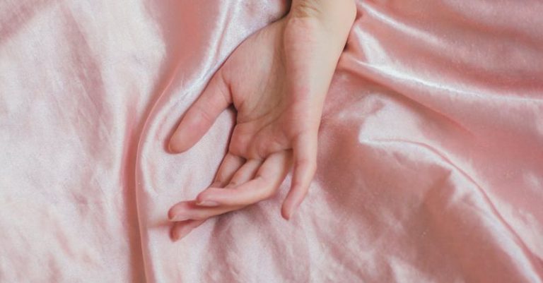 Sensitive Skin - Top view of hand of crop anonymous female on soft silk creased bed sheet at home