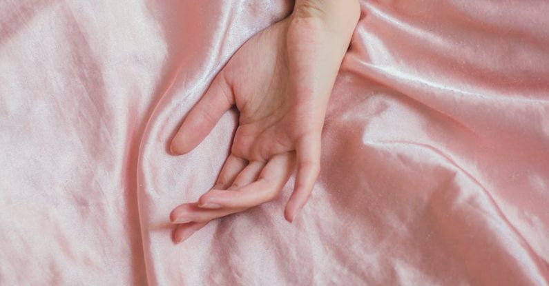 Sensitive Skin - Top view of hand of crop anonymous female on soft silk creased bed sheet at home