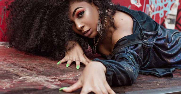Strong Nails - Beautiful Woman with Long Curly Hair Laying on Garbage Container