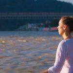 Meditation Tips - A woman sitting on a bench in front of a river