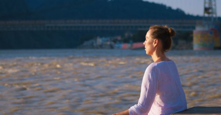 Meditation Tips - A woman sitting on a bench in front of a river
