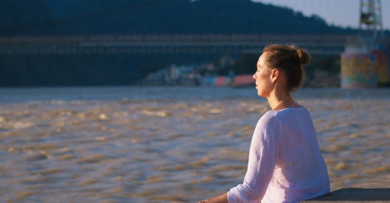 Meditation Tips - A woman sitting on a bench in front of a river